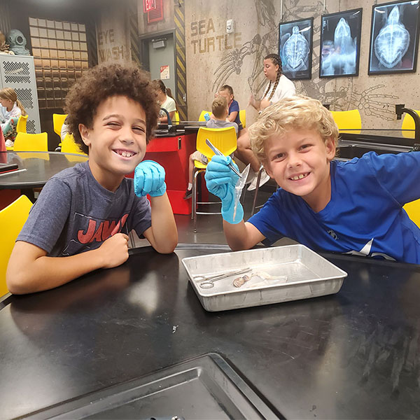 two boys in the learning lab wearing gloves smiling at the camera