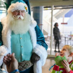 Little boy eating a pancake while smiling up at Santa wearing a blue suit while parents watch at The Florida Aquarium