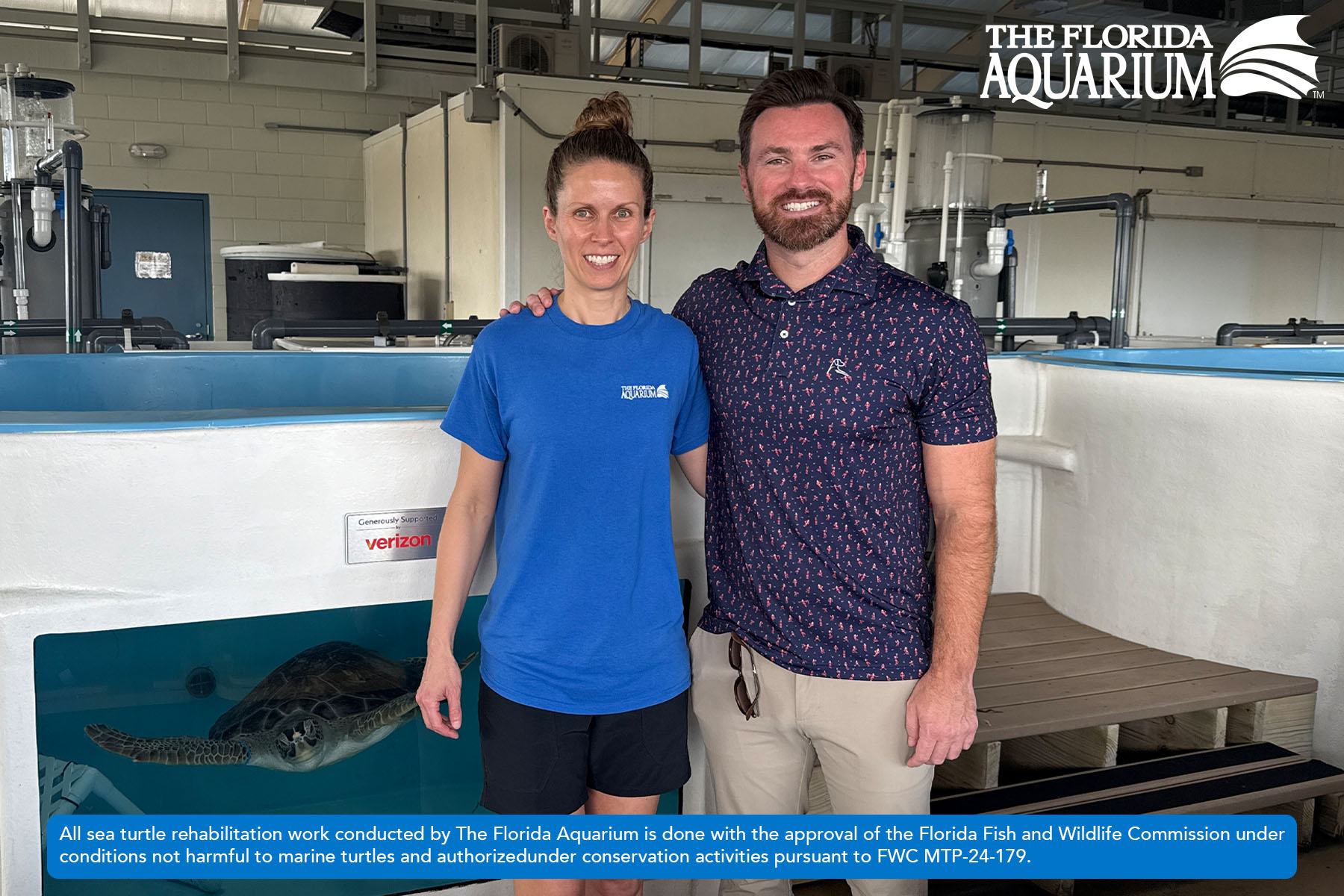 Ashley Riese, Director, Sea Turtle Conservation Program at The Florida Aquarium (left) with Ed Buckley (right) standing in front of deep dive pool with Buckley the rescued green sea turtle swimming behind them at The Florida Aquarium's Sea Turtle Rehabilitation Center in Apollo Beach, FL